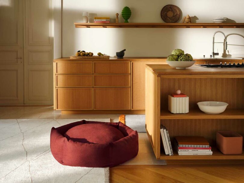 A red circular Luoto dog bed placed in a clean, modern living room with contemporary furniture.