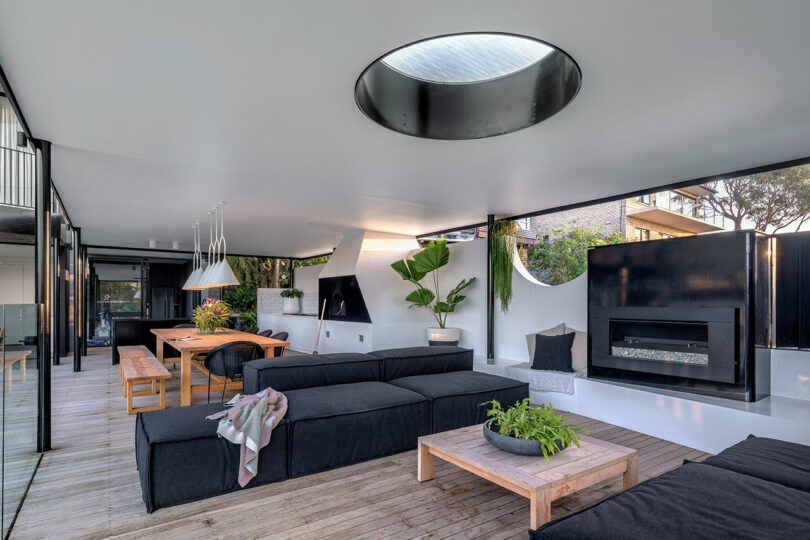 Modern open-plan living room with white walls, black sectional sofa, and a circular skylight.