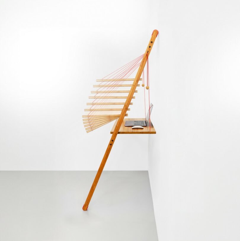 Modern wall-mounted desk with wooden slats and red tension strings used as a display shelf.