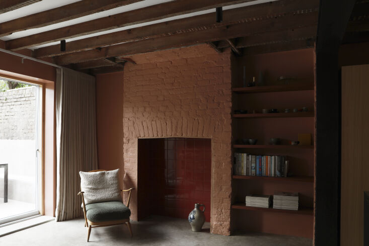 Earthy-pink kitchen with glossy red tiles and vintage Ercol chair.