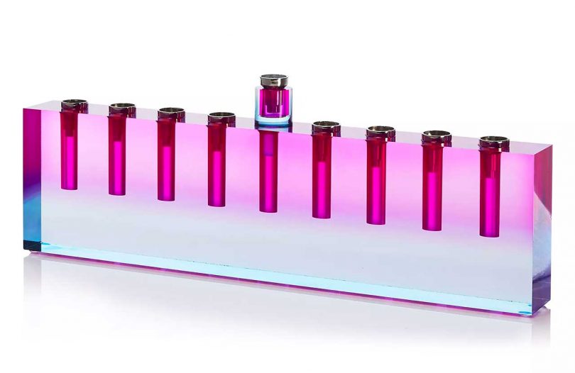A pink and blue prism glass menorah that creates colorful reflections.