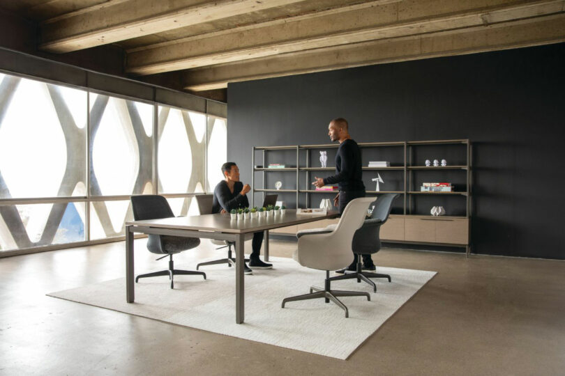 Two people conversing in an industrial-style office with exposed wood beams and modern furniture.