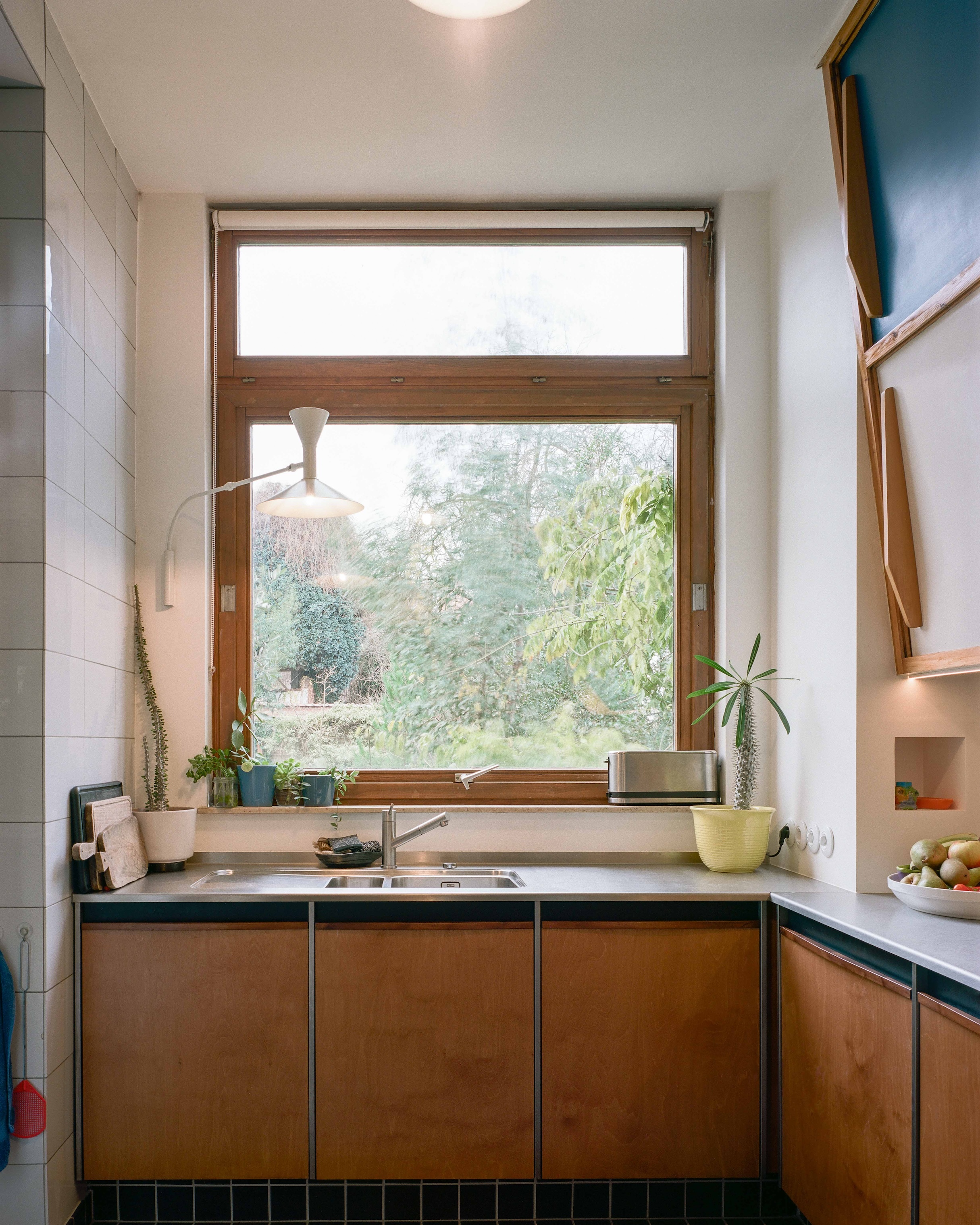 Kitchen sink area featuring a Franke faucet, a large window, and a Le Corbusier Lampe de Marseille wall sconce.