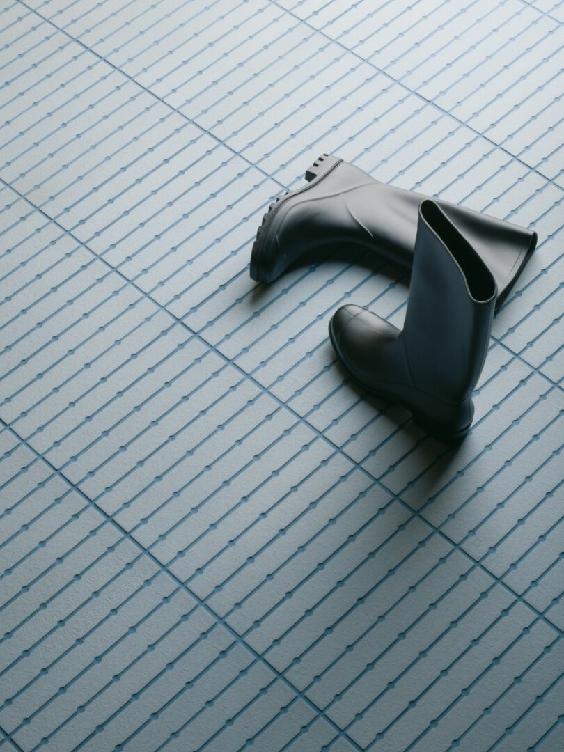 Black rubber boots standing on a light blue tiled floor with a geometric grid and dot pattern.