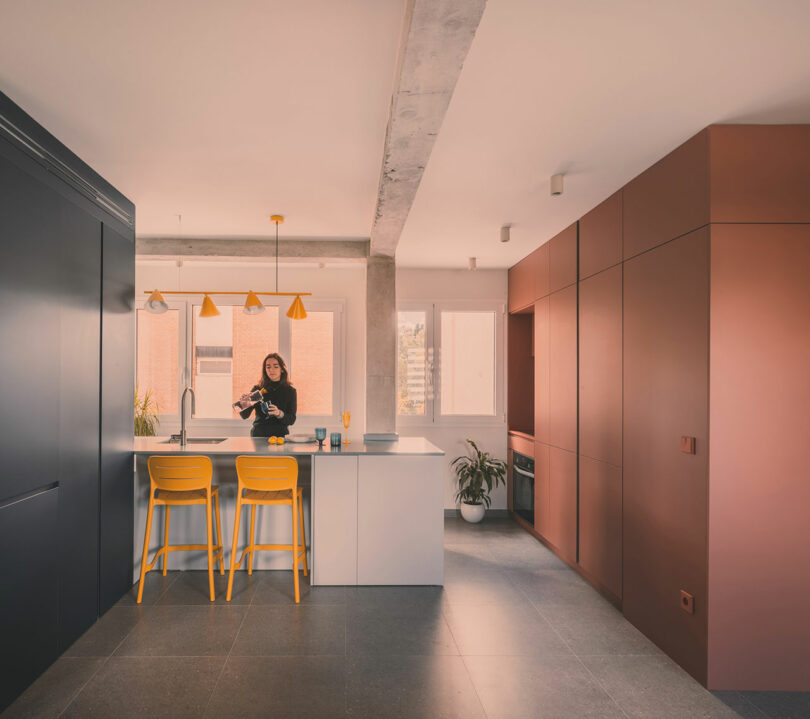 A modern kitchen island with yellow stools and dark cabinetry under bright natural light from large windows.