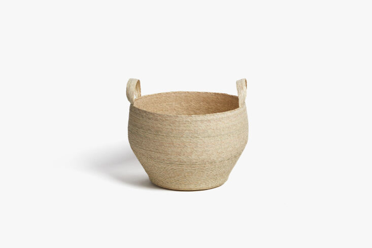 Handwoven palm leaf floor basket used for storage in a minimalist room.