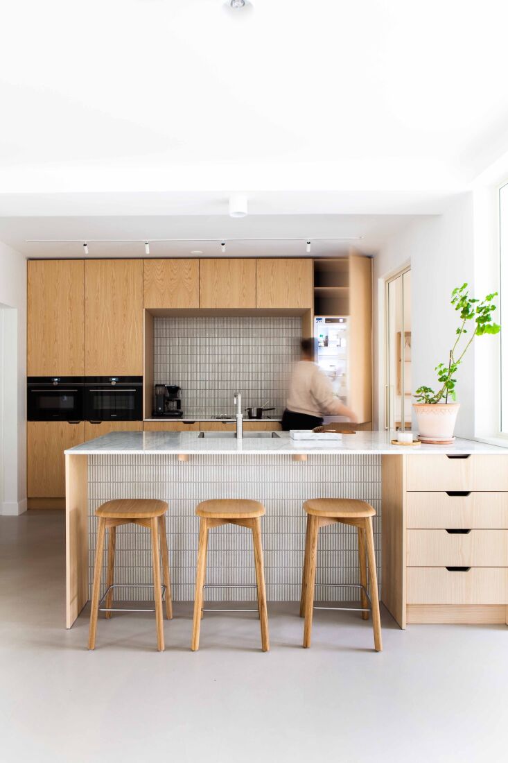 A person using a refrigerator in a modern Scandinavian-style kitchen with light wood cabinetry.