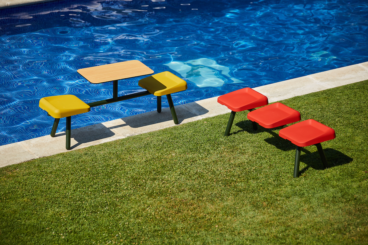Modern outdoor patio featuring colorful Boln Slim stools and a table beside a swimming pool on a sunny day.