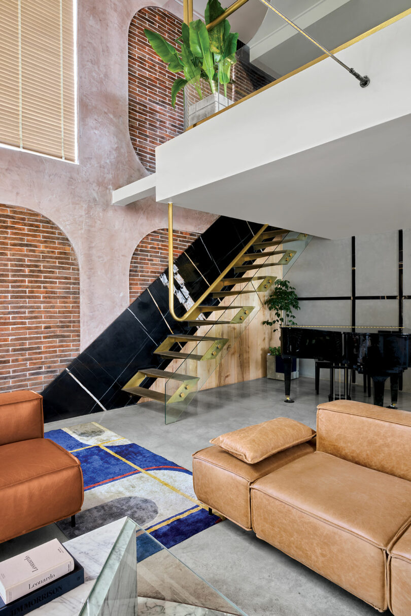 A sculptural black and gold staircase next to a grand piano and exposed brick wall.