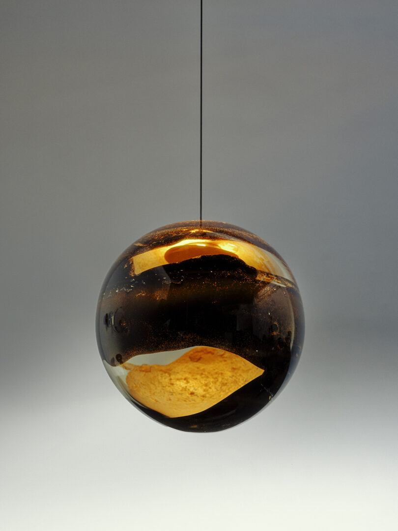 A spherical glass pendant with dark amber swirls suspended by a minimal black cord.