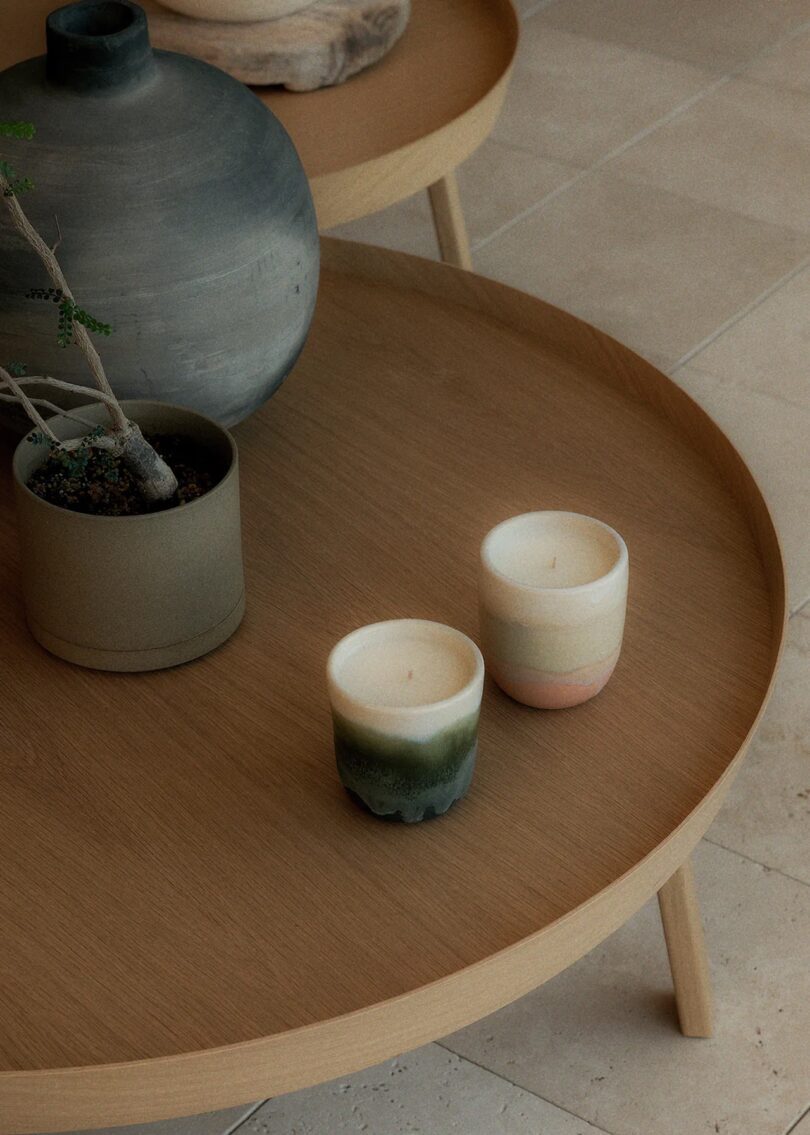 Two ceramic candles in muted pink and green tones on a wooden table.