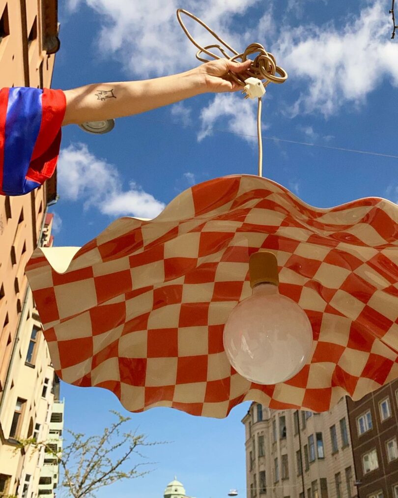 A checkered pendant lamp held against a bright blue urban sky.
