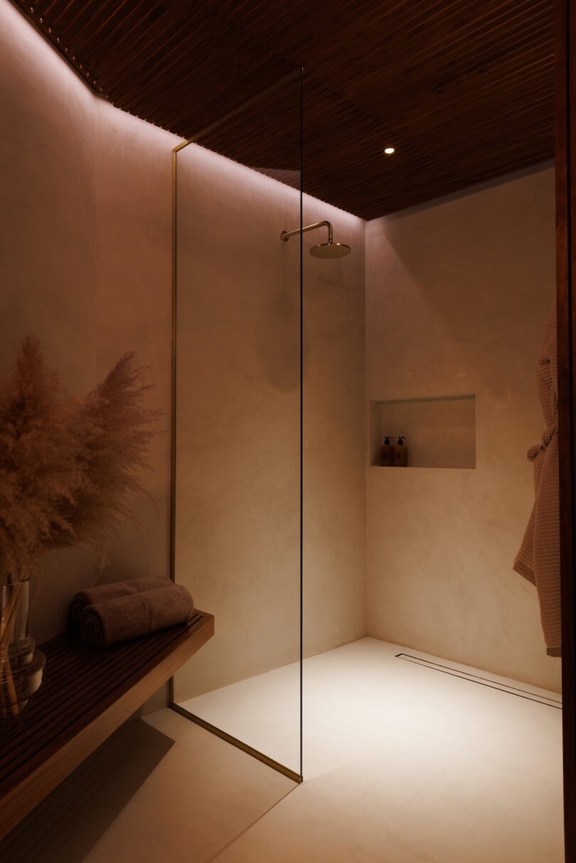 Minimalist walk-in shower with glass partition, wood bench, and ambient lighting.