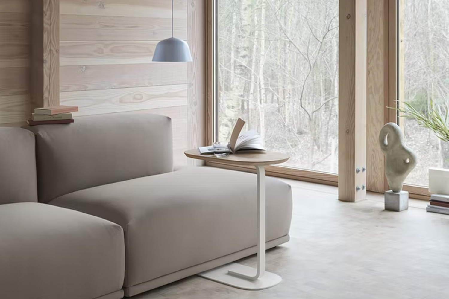 Minimalist living room with a beige sectional sofa and a sleek C-shaped side table in front of a window.