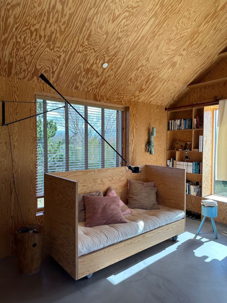 A minimalist living space with plywood walls, a concrete floor, and a modern daybed.