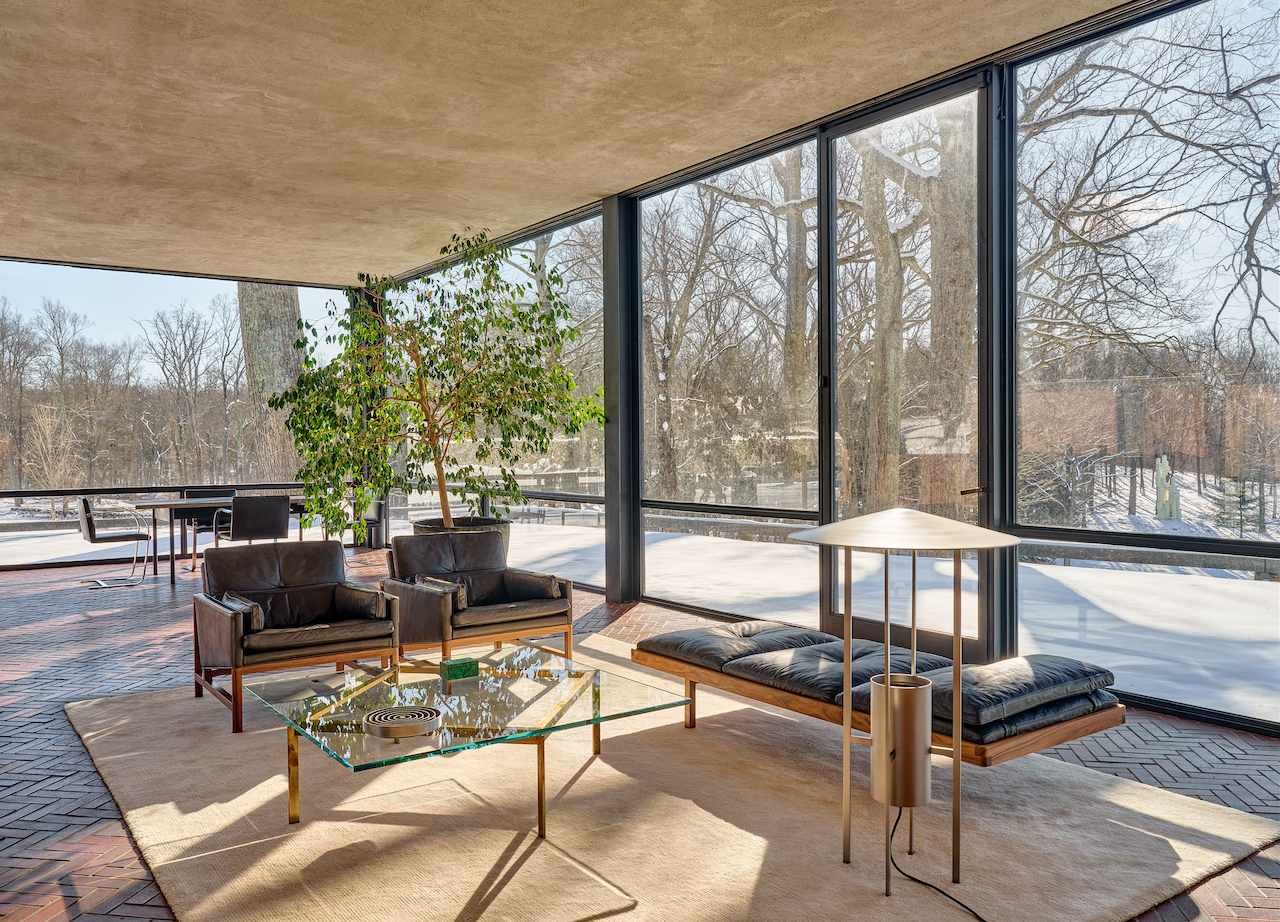 A mid-century modern living room with floor-to-ceiling glass windows looking out onto a snowy winter forest.