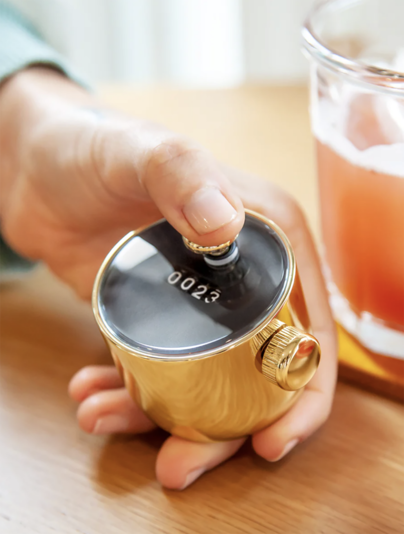 A close-up of a hand holding a polished gold mechanical tally counter.