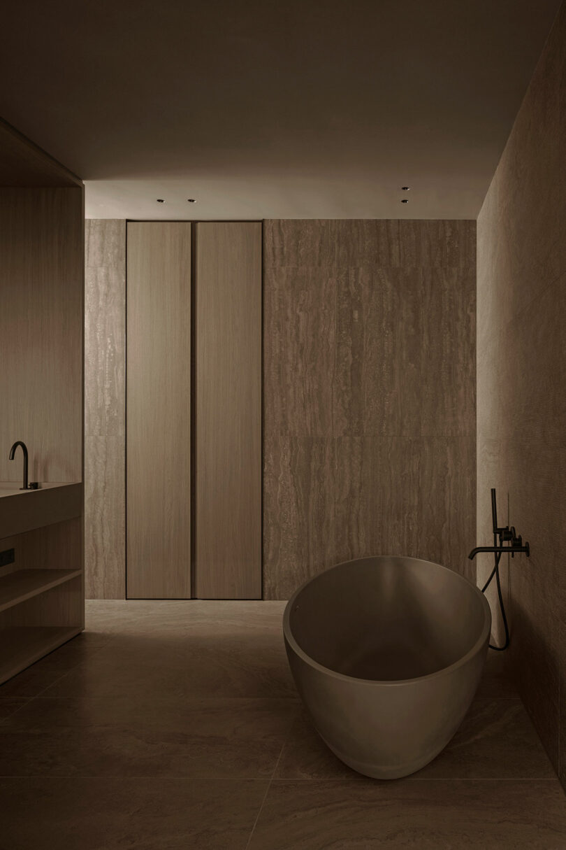 Minimalist bathroom with a freestanding oval bathtub, wood-paneled walls, and stone flooring.