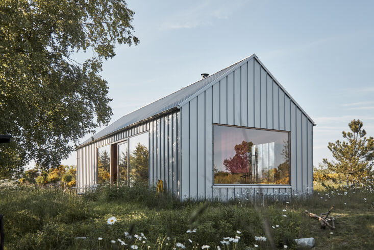 Exterior view of a house clad in dark lacquered steel plates with a matching roof.