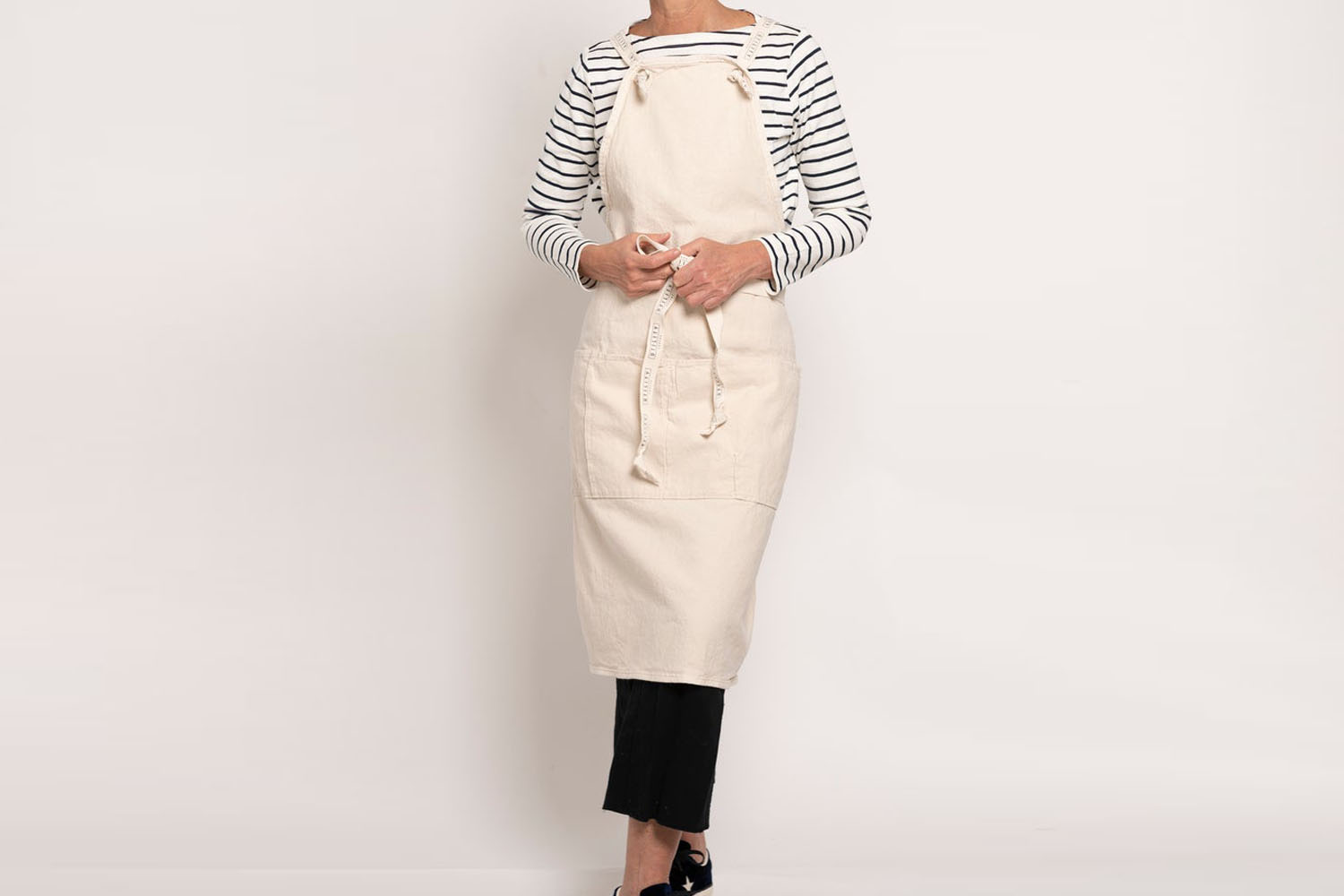 A full-length natural canvas utility apron with large front pockets.