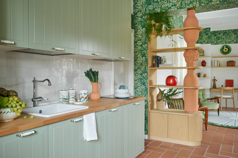 Kitchen with sage green cabinets, wooden countertops, and leafy wallpaper.