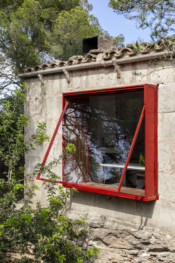 A bright red metal-profile bow window framing the landscape of a pine forest and old quarry.