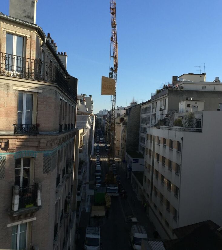 Construction workers using a crane to lower prefabricated sections onto a Paris rooftop.