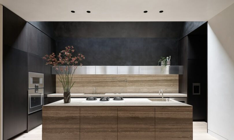 A luxury kitchen with a massive marble island, dark wood cabinetry, and minimalist shelving.