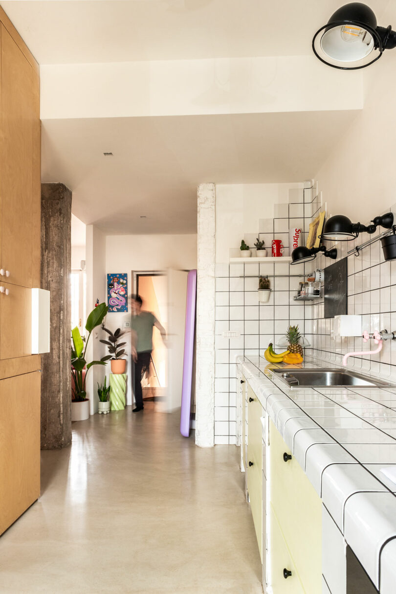 Modern kitchen with white tiles, yellow cabinetry, and a thick wooden structural column.