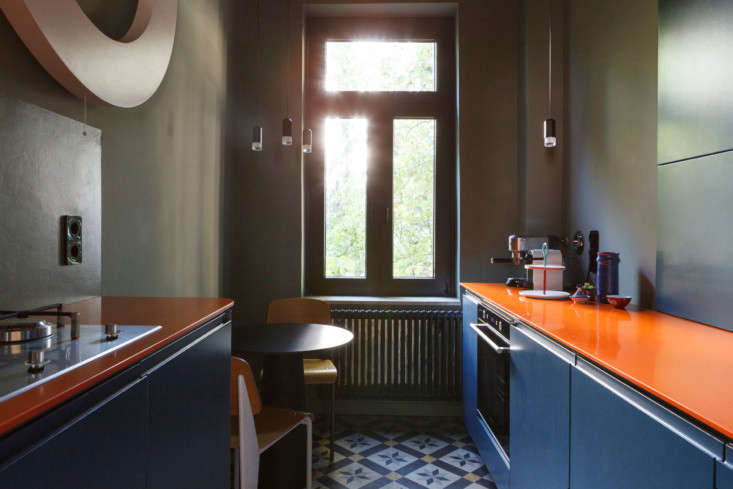 Modern kitchen with bold orange Corian countertops and dark moody cabinetry.