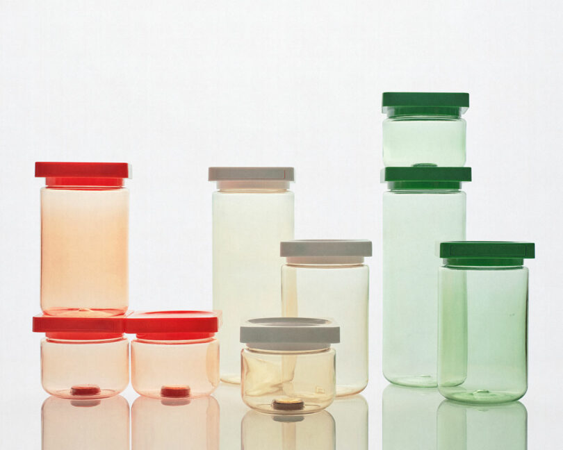 Transparent plastic jars with red, gray, and green lids arranged on a reflective surface against a clean white background.