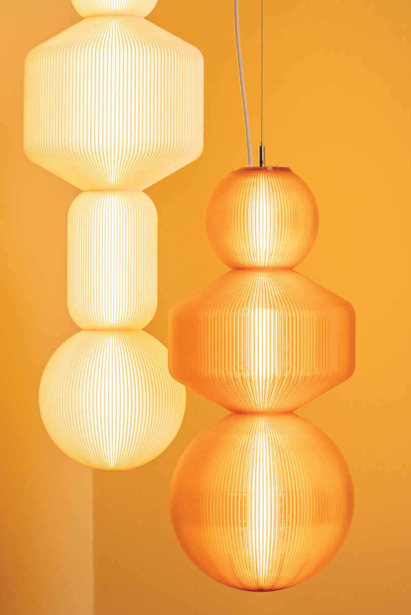 One white and one orange geometric pendant light hanging side-by-side against a yellow background.