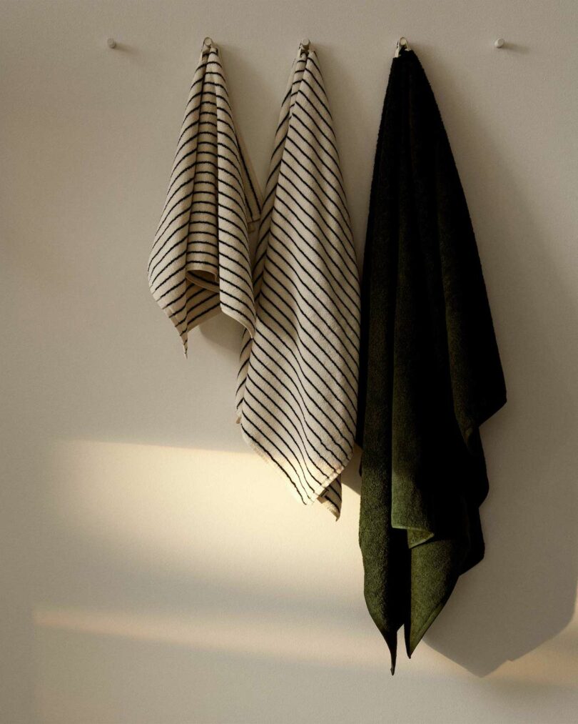 A collection of green and white striped and solid dark green towels hanging on a wall.