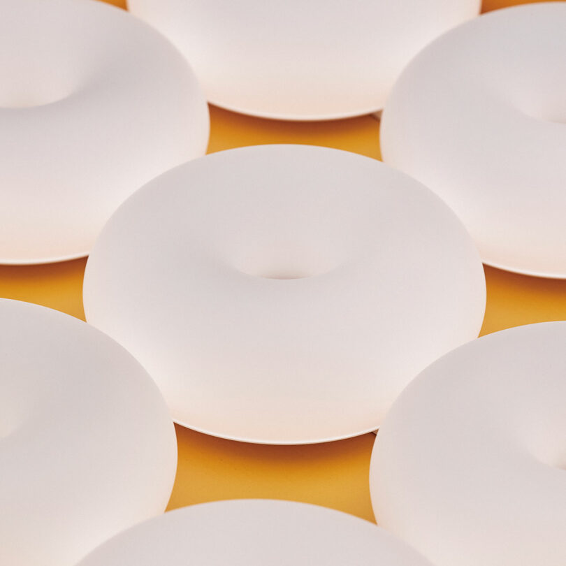 Multiple white donut-shaped lamps arranged in rows on a bright yellow background.