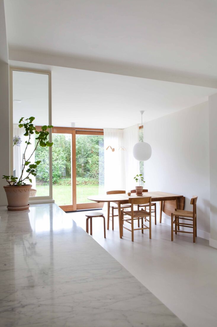 An oiled oak drop-leaf dining table with designer chairs in a minimalist setting.