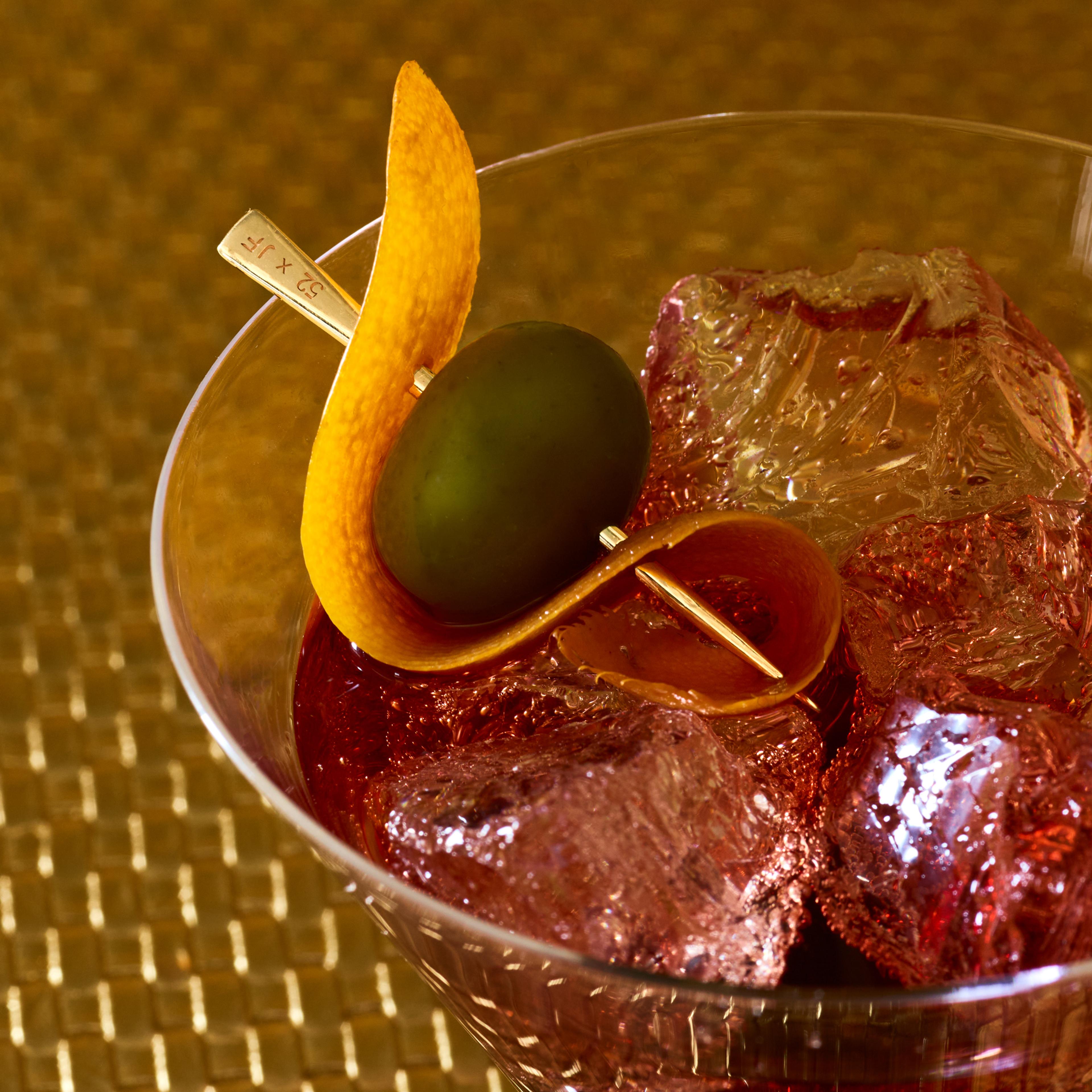 A 14k gold toothpick used as a cocktail pick inside a martini glass.