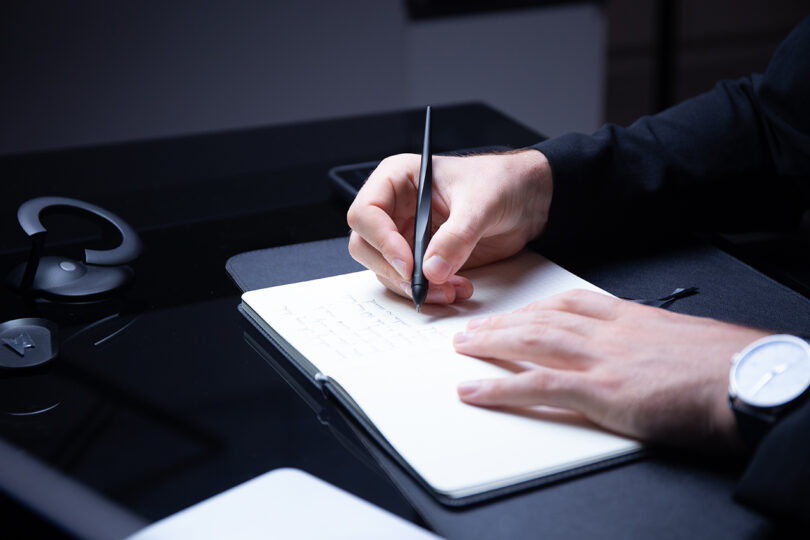 A close-up of a person writing in a notebook using the Novium Hoverpen.