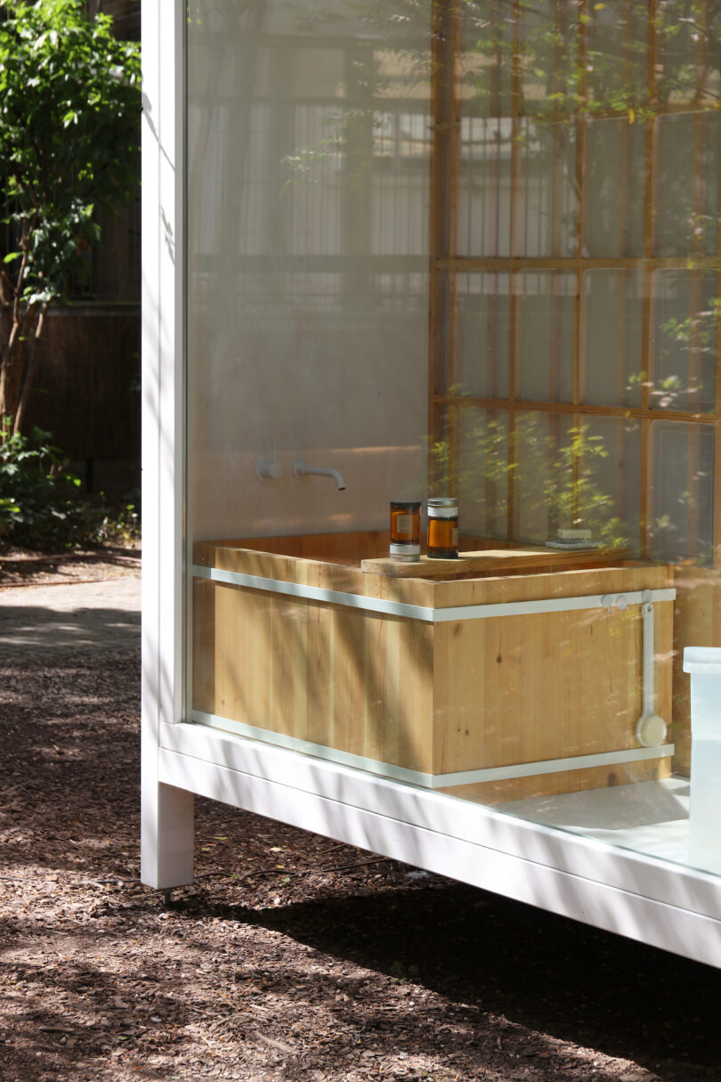 A wooden Japanese soaking tub inside a glass-walled modular unit with trees visible outside.