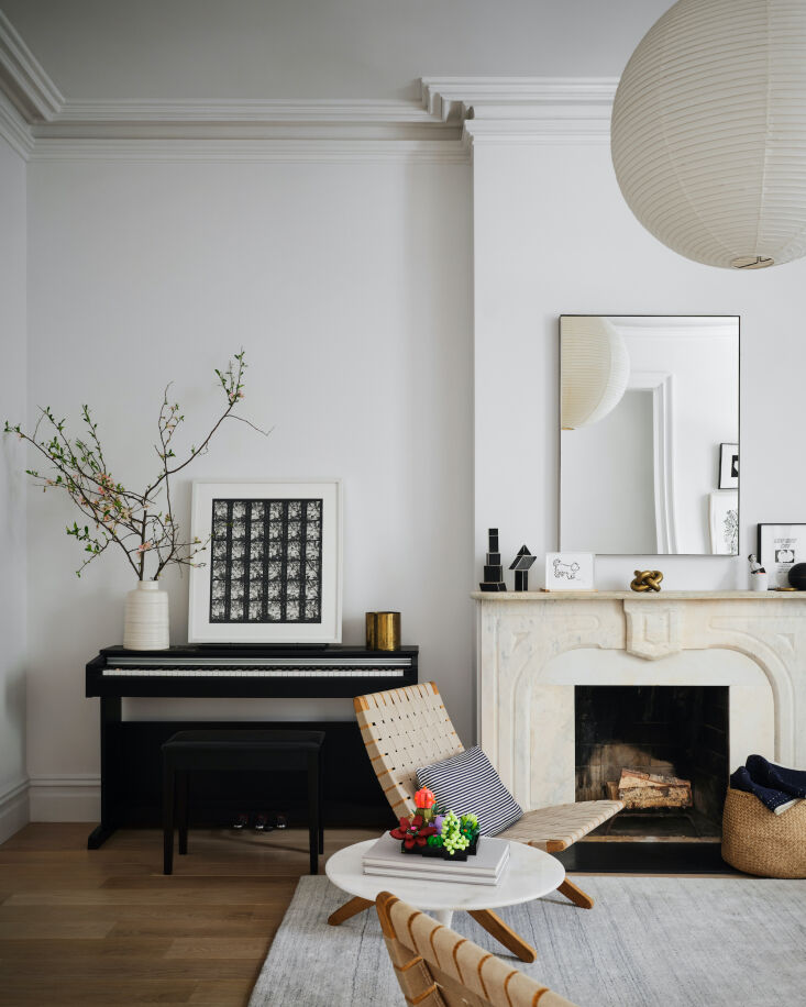 Elegant living room with a classic white fireplace, a black piano, and modern woven chairs.