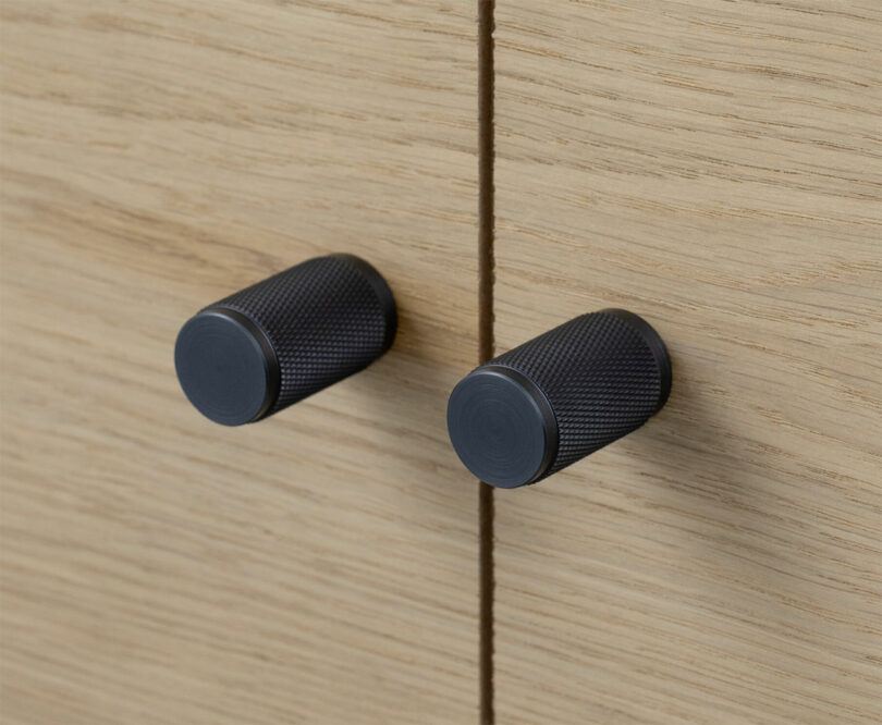 Close-up of matte black knurled cabinet pulls on a dark drawer.