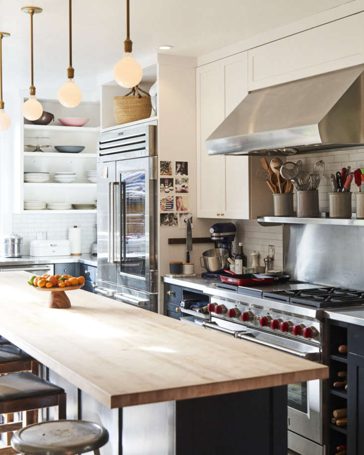 A kitchen wall with open shelving for tools, a speed rack next to the stove, and dedicated rolling pin cubbies.