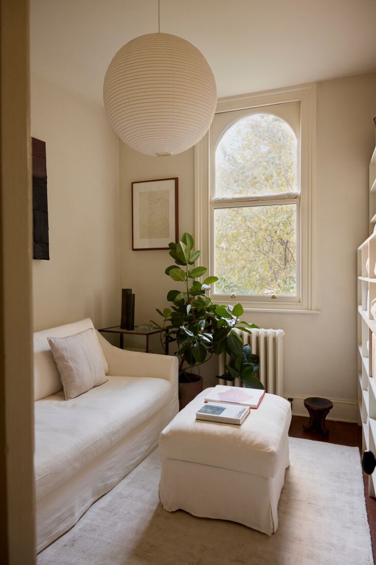 Bright minimalist living room featuring a white sofa, an arched window, and a large potted plant.