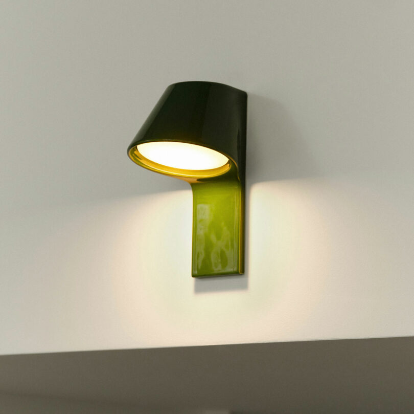 A green wall-mounted lamp casting a soft upward glow against a white tiled wall.