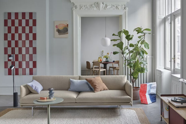 A grey Muuto Outline 2-seater sofa with thin metal legs and slim armrests in a bright room.