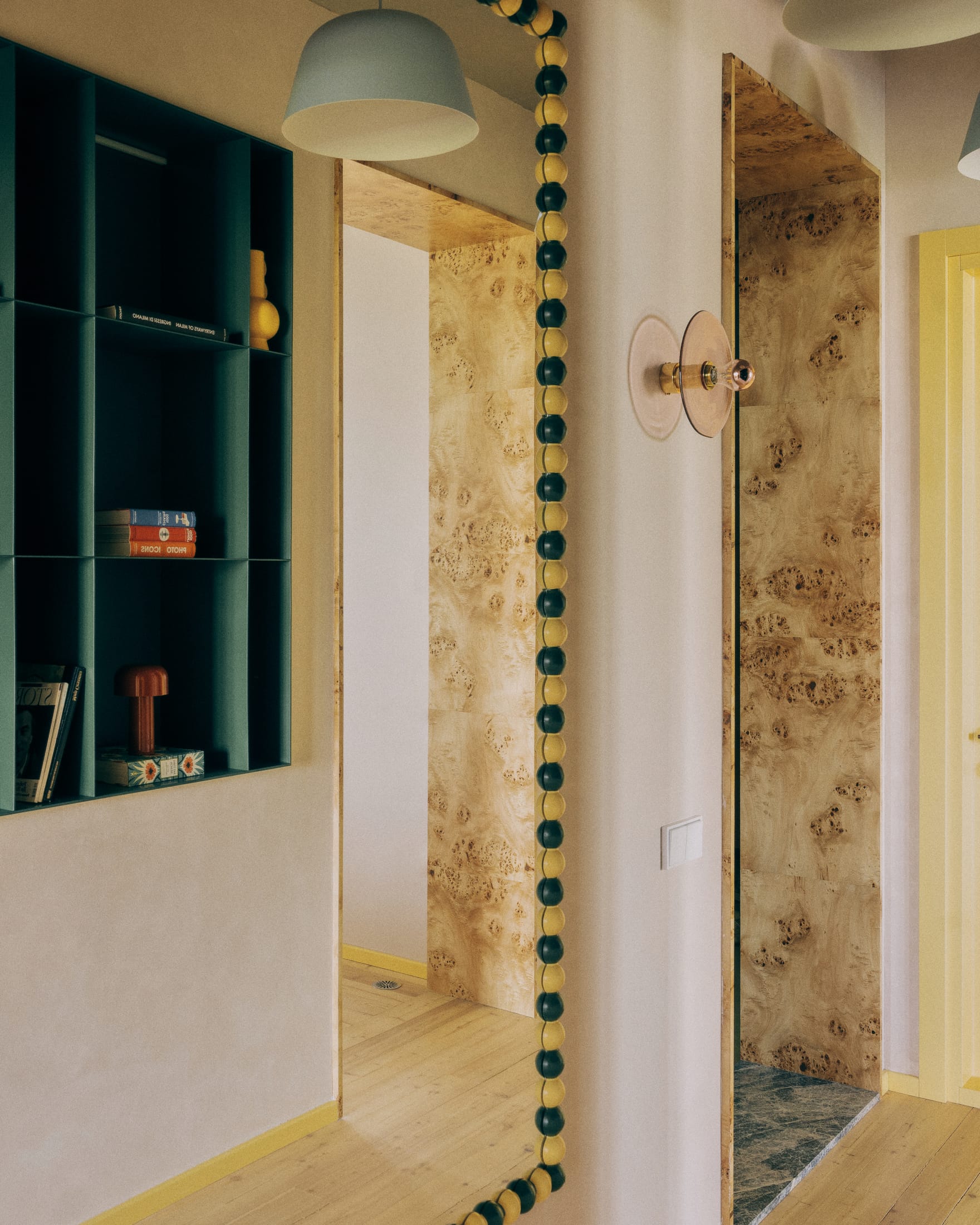An entryway featuring teal built-in shelves, a wooden-framed mirror, and a minimalist pendant light.