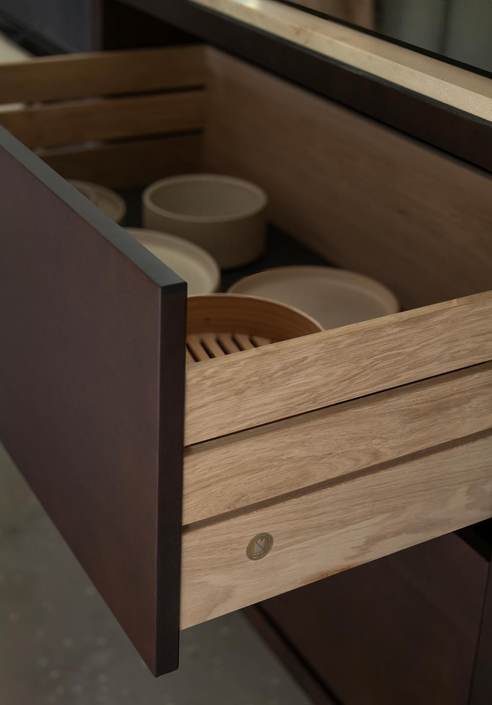 Close-up of a minimalist kitchen drawer with organized ceramic bowls and light wood interior.