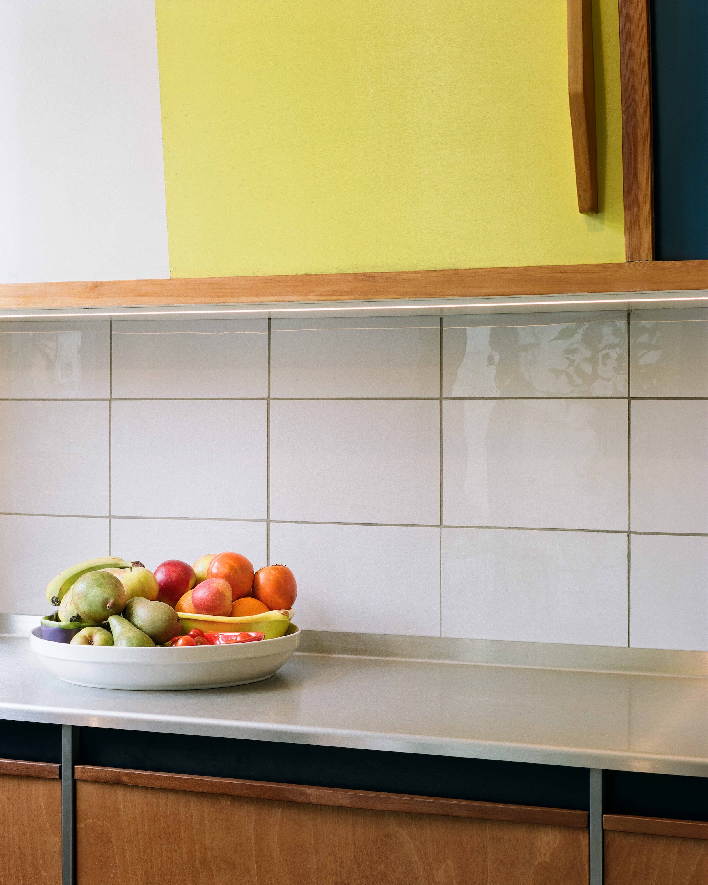 A close-up of a stainless steel countertop meeting a backsplash of white Marbrite milk glass tiles.