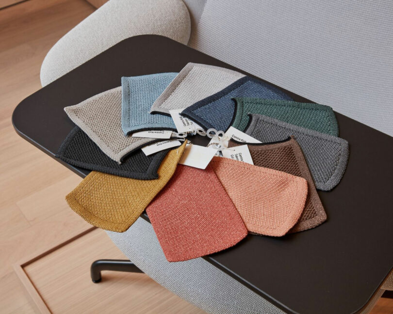 Textured fabric swatches in neutral tones fanned out on a table next to a modern upholstered chair.