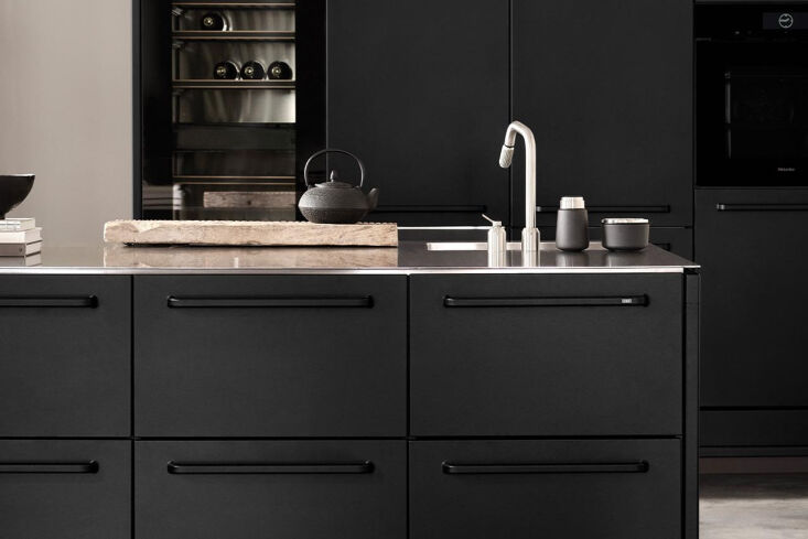 Sleek black Vipp V1 kitchen modules with integrated cooktop and stainless steel sink.