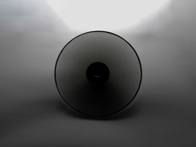 A dark circular glass object with a luminous gradient halo against a gray background.